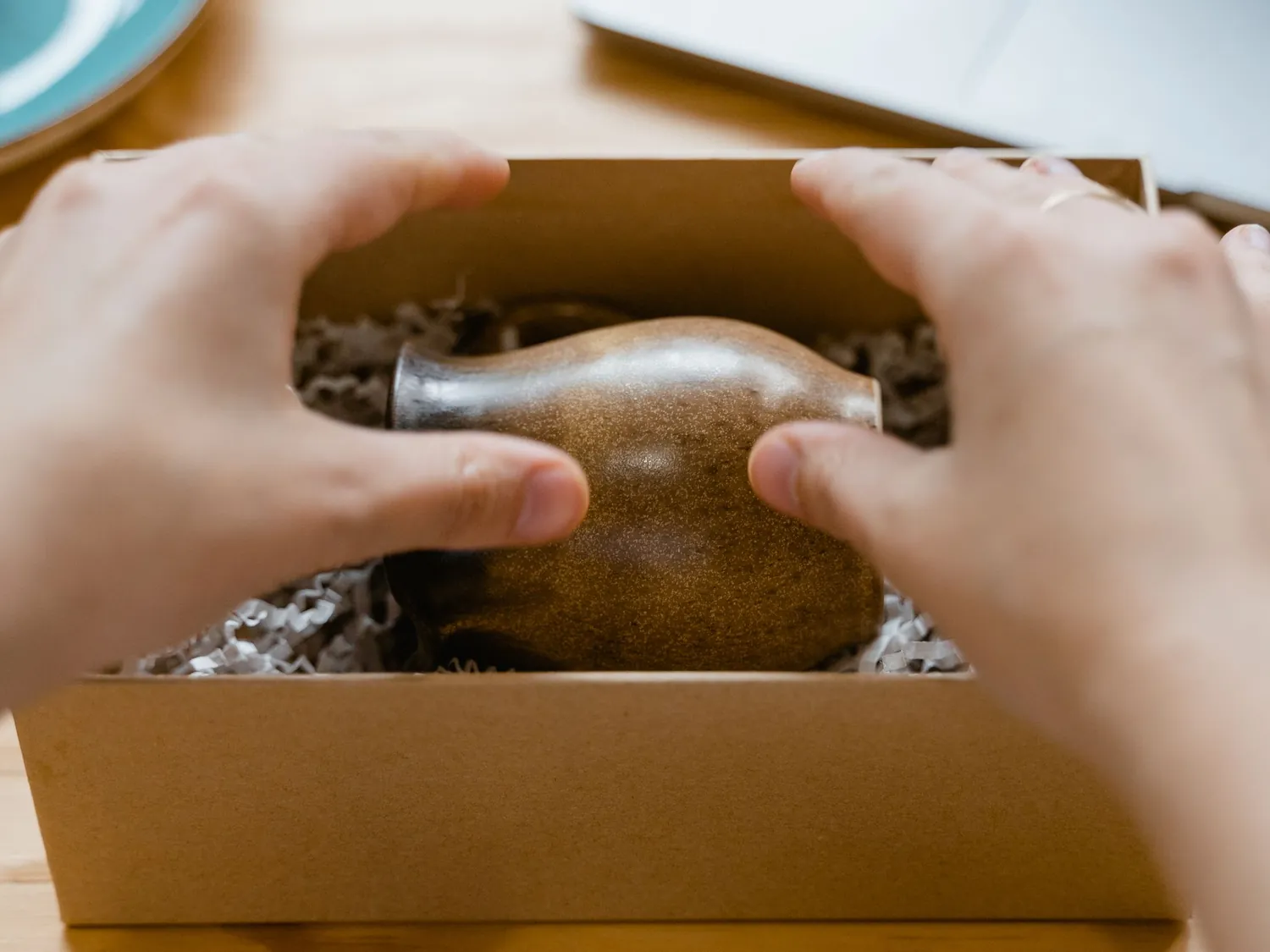 Hands packing a ceramic vase into a cardboard shipping box